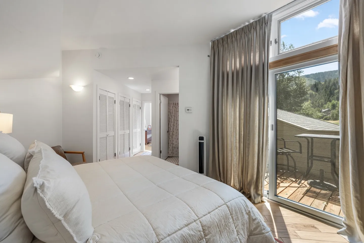 Bedroom with a white bed, closet louvered doors, and sliding glass doors leading to a private outdoor balcony with chairs.