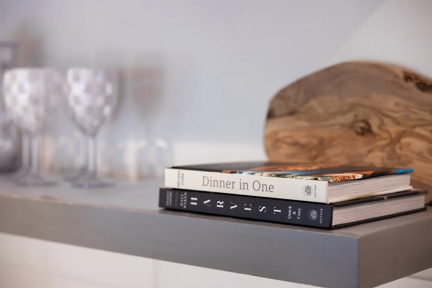 Close-up of a gray open shelf displaying cookbooks, a wooden board, and patterned glassware.