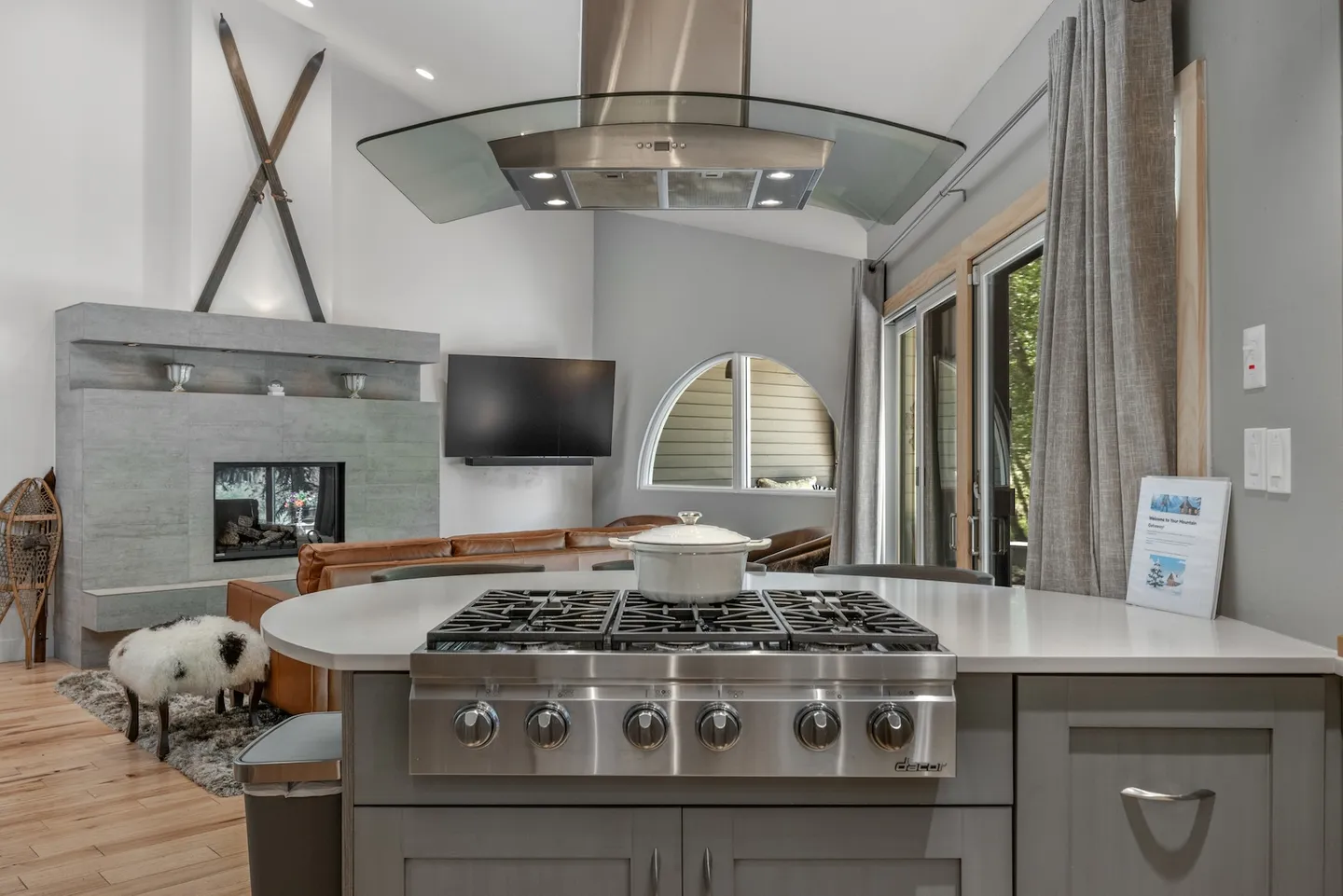 Kitchen island with a stainless steel gas cooktop and glass range hood, overlooking an open-concept living room with a fireplace and television.