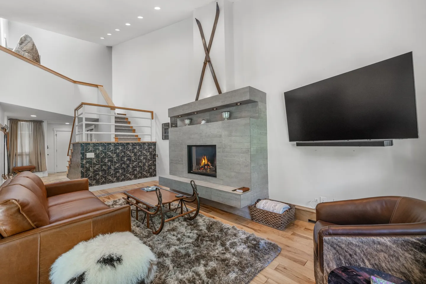 Living room with high ceilings, a modern gray fireplace, leather seating, and decorative wooden skis mounted above the hearth.