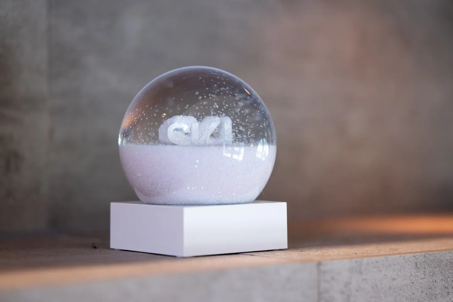 A close-up of a decorative snow globe with a white rectangular base sitting on a stone-like surface.