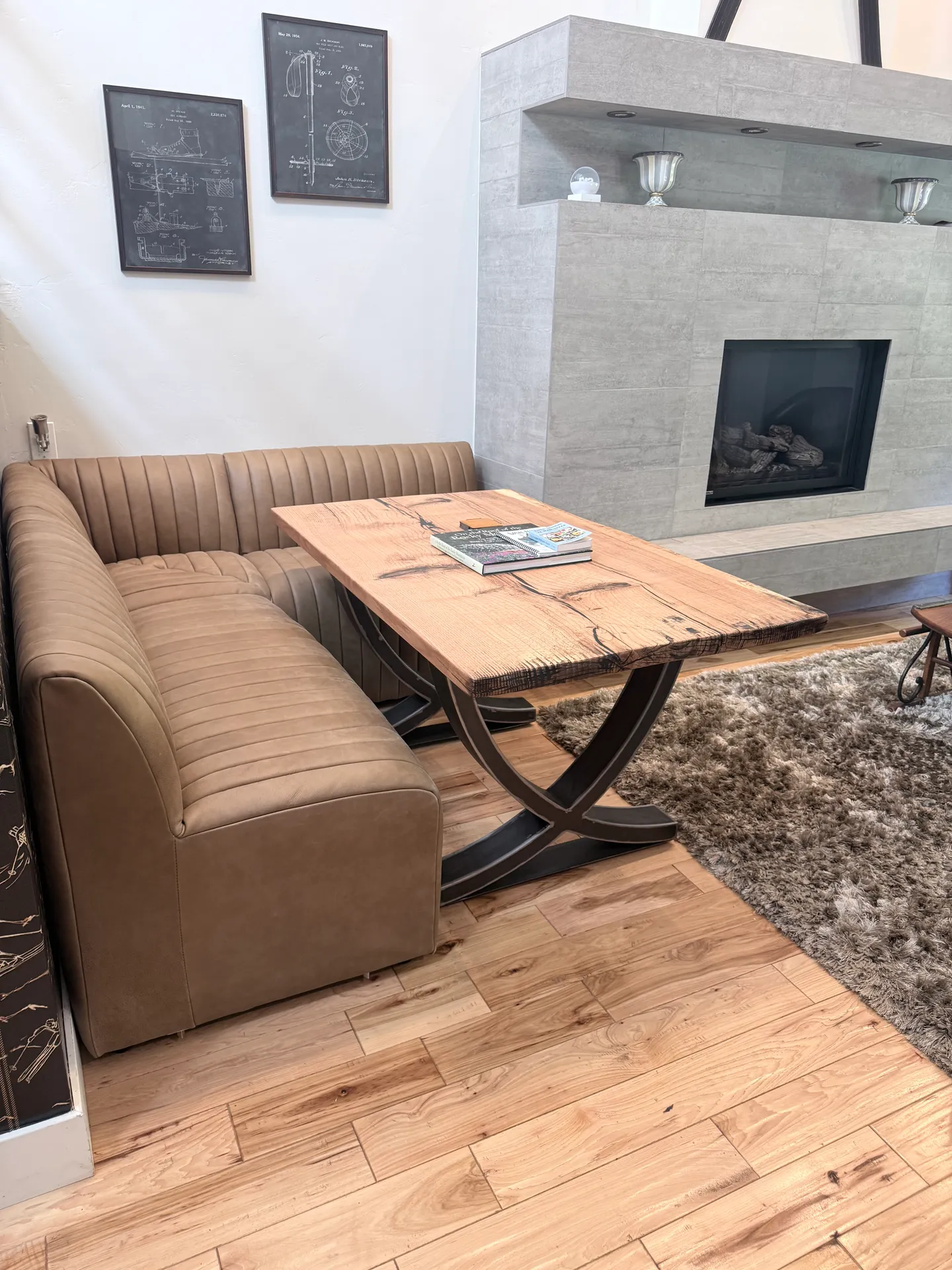 A corner banquette seating area with a leather-like upholstered bench and a wood table next to a tiled modern fireplace.