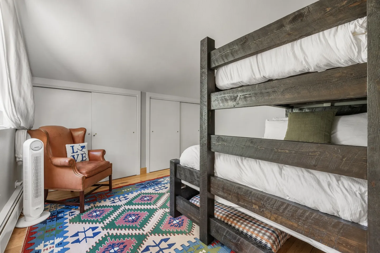 Bedroom featuring rustic wooden bunk beds, a geometric patterned rug, and a leather armchair in the corner.