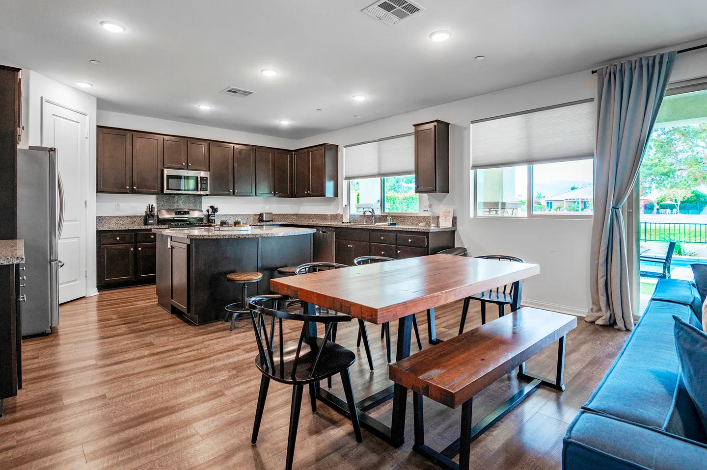 Open-concept dining area and kitchen with dark wood cabinetry, an island, and a wooden dining table with bench and chairs.