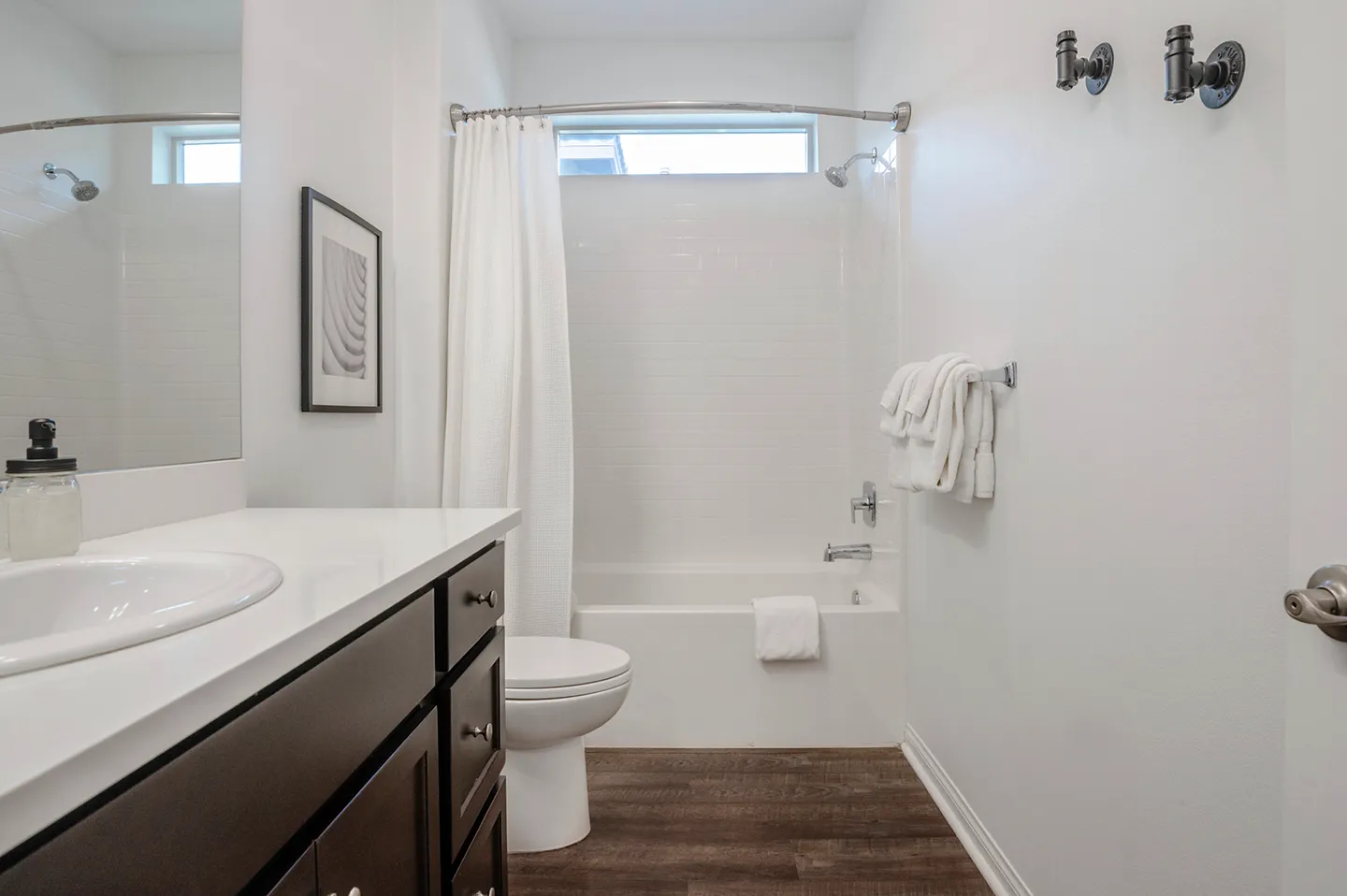 Bathroom with dark vanity, white countertop, toilet, and combination bathtub and shower with white tile.
