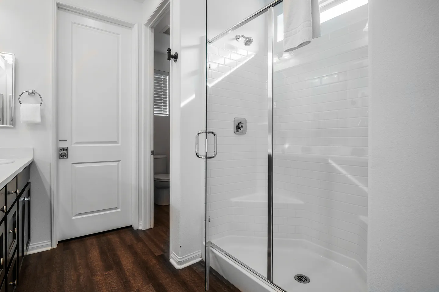 Bathroom with a glass-enclosed walk-in shower featuring white subway tile, adjacent to a dark vanity and white doors.
