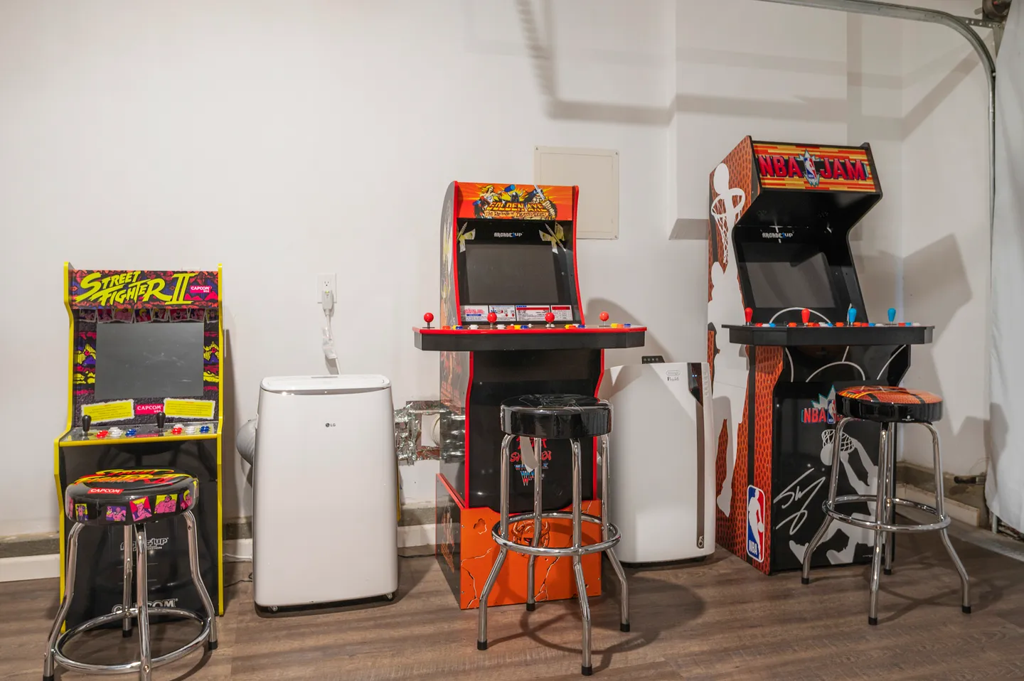 Row of retro-style arcade cabinets and matching stools set against a white wall.