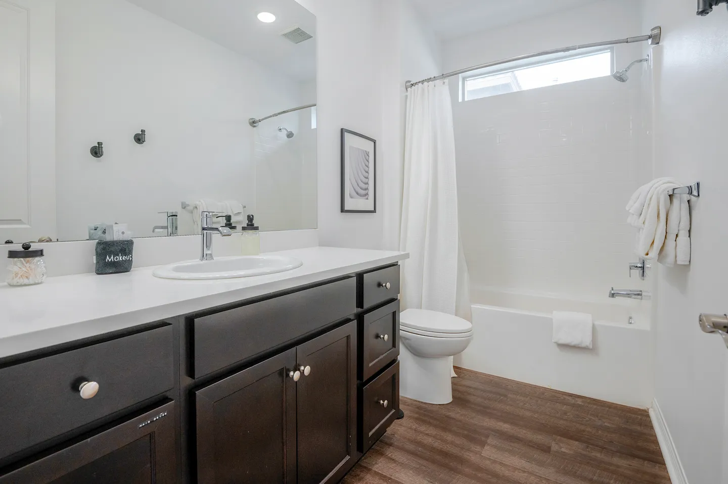 Bathroom with a dark vanity, white countertop, large mirror, toilet, and combination bathtub and shower with white tile.