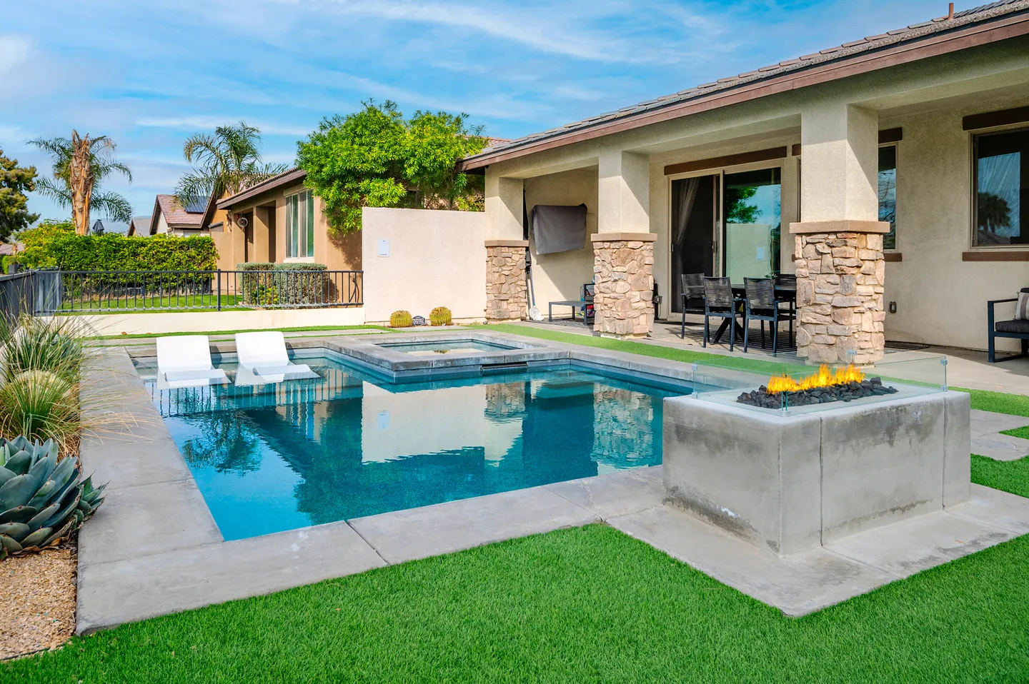 Backyard patio with an in-ground swimming pool, attached hot tub, modern gas fire pit, and synthetic lawn.