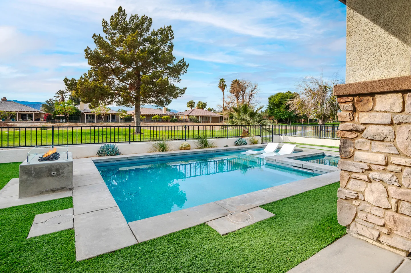 Outdoor swimming pool and hot tub with a modern concrete fire pit in a backyard overlooking a golf course.