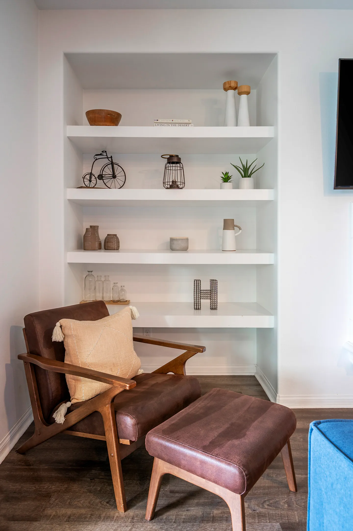 A leather armchair and matching ottoman positioned in front of built-in recessed white shelving decorated with various ornaments.