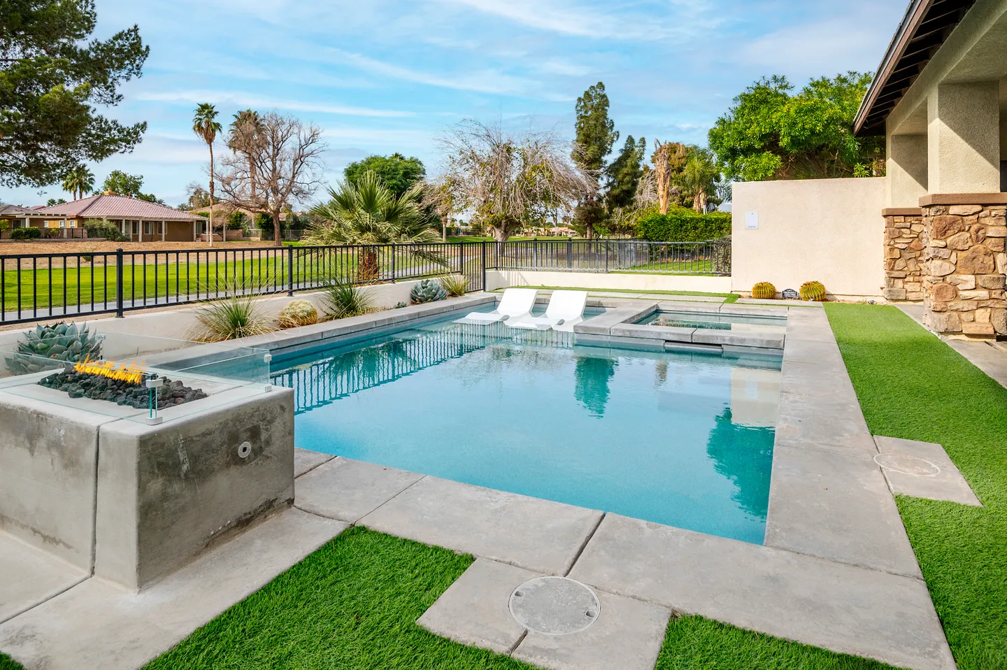 Outdoor swimming pool with built-in hot tub, in-pool lounge chairs, and a fire pit bordering a golf course.