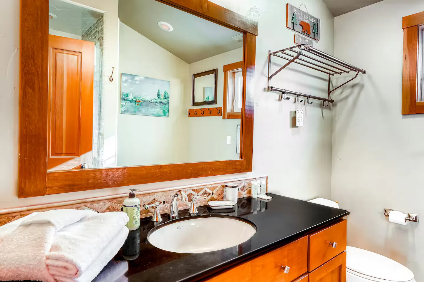Bathroom with a wood-framed mirror over a black vanity countertop with an undermount sink and a metal towel rack on the wall.