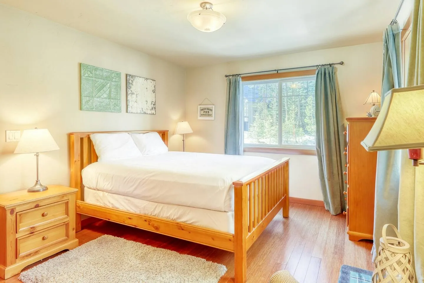 Bedroom with a wooden bed frame, matching nightstand and dresser, a picture window with curtains, and wood-look flooring.
