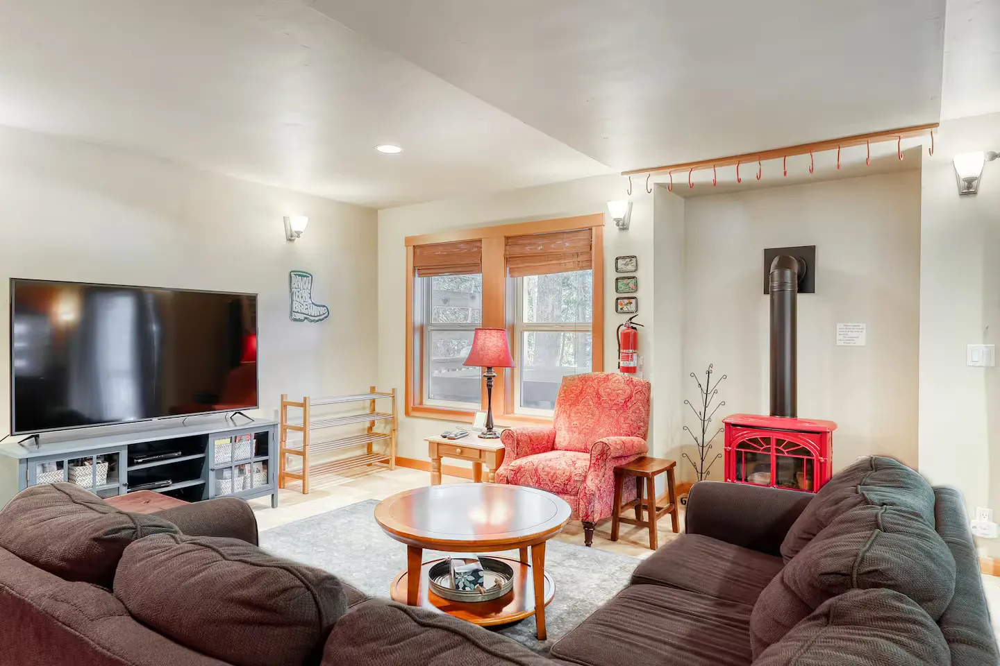 Living room with brown sofas, a round wooden coffee table, a red armchair, a flat-screen TV, and a red wood-burning stove.