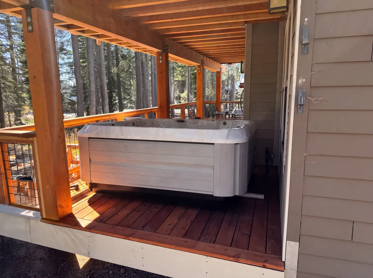 A hot tub situated on a covered wooden deck with views of tall pine trees.