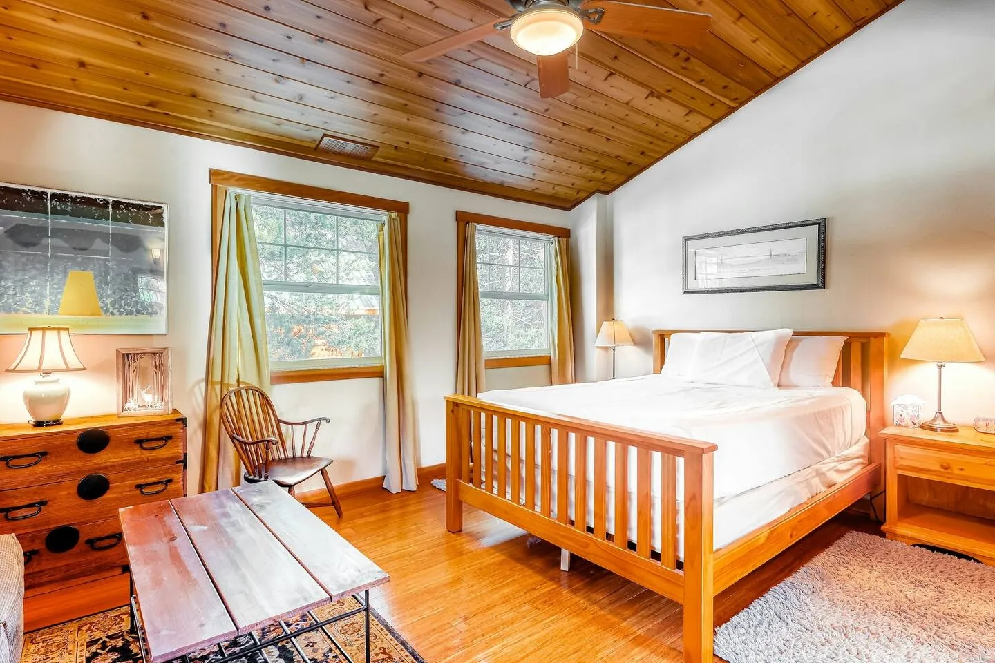 Bedroom featuring a wooden slat bed frame, wood-paneled ceiling with a fan, wood-look flooring, and windows with drapes.