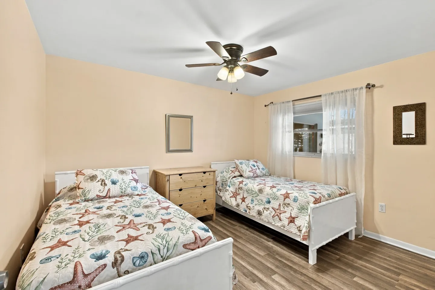 Bedroom featuring two twin beds with coastal-themed bedding, a wooden dresser between them, and a ceiling fan.