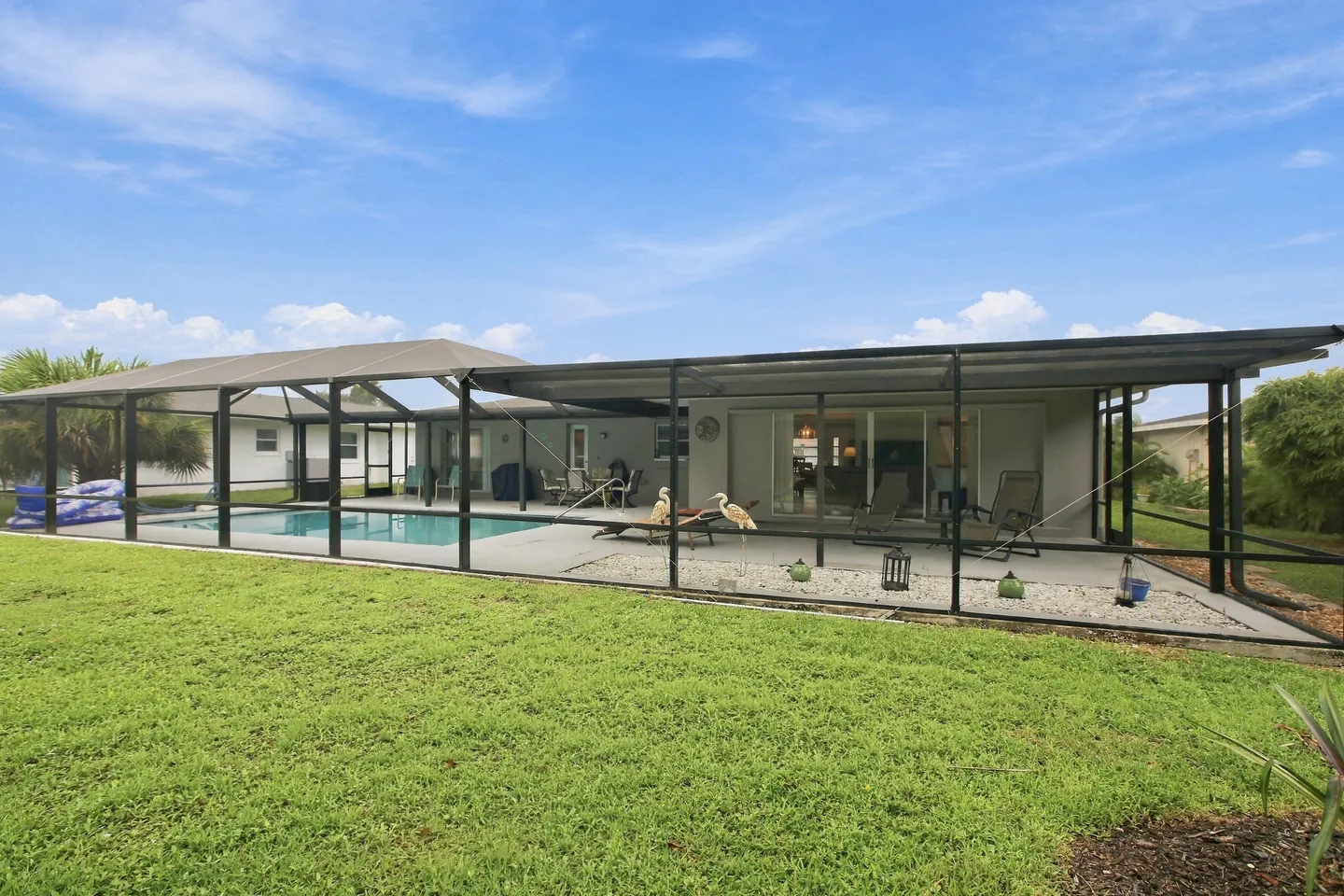 Exterior view of a home with a large screened-in pool cage and patio beside a grassy lawn under a blue sky.