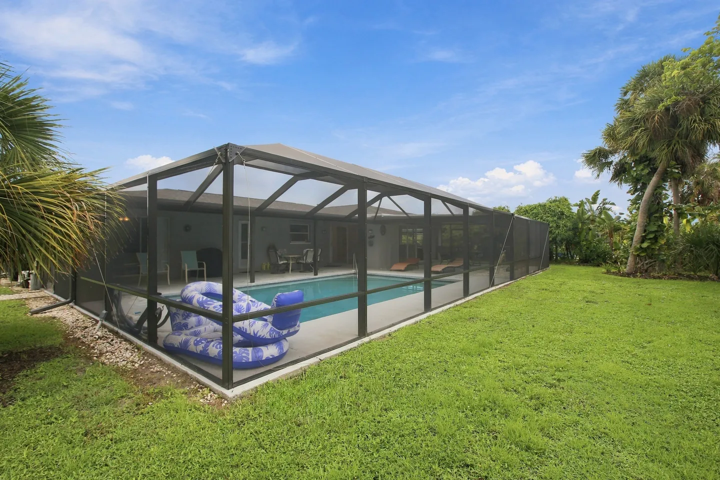 Exterior view of a screened pool cage with a swimming pool inside, surrounded by a grassy lawn and palm trees under a blue sky.