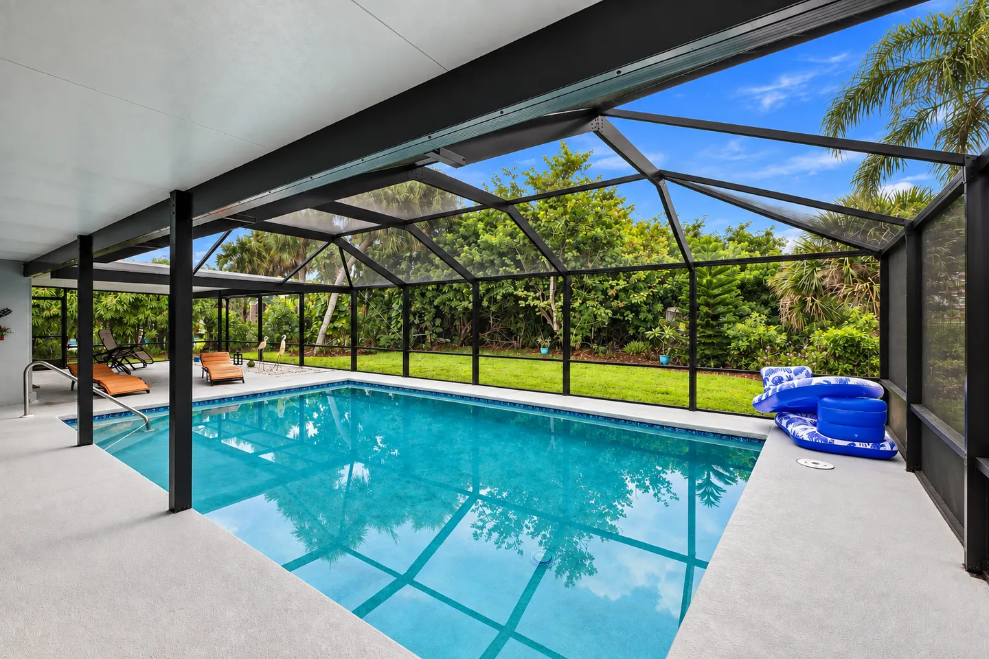 Swimming pool inside a screened enclosure next to a covered patio with lounge chairs and pool floats.