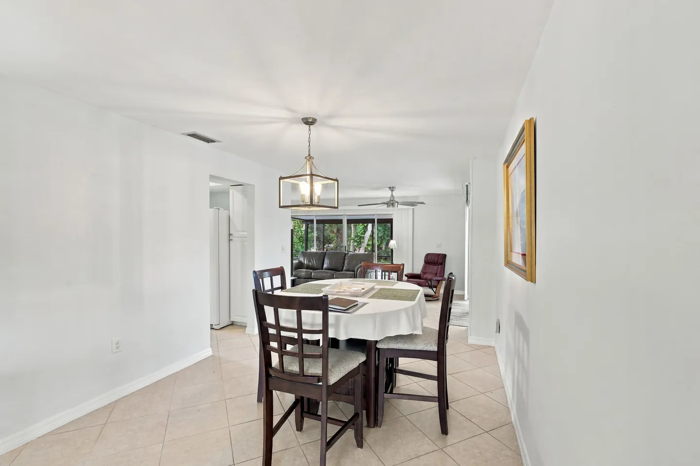 Dining area with a round table, dark wooden chairs, and a hanging lantern light fixture, leading to an open living room.