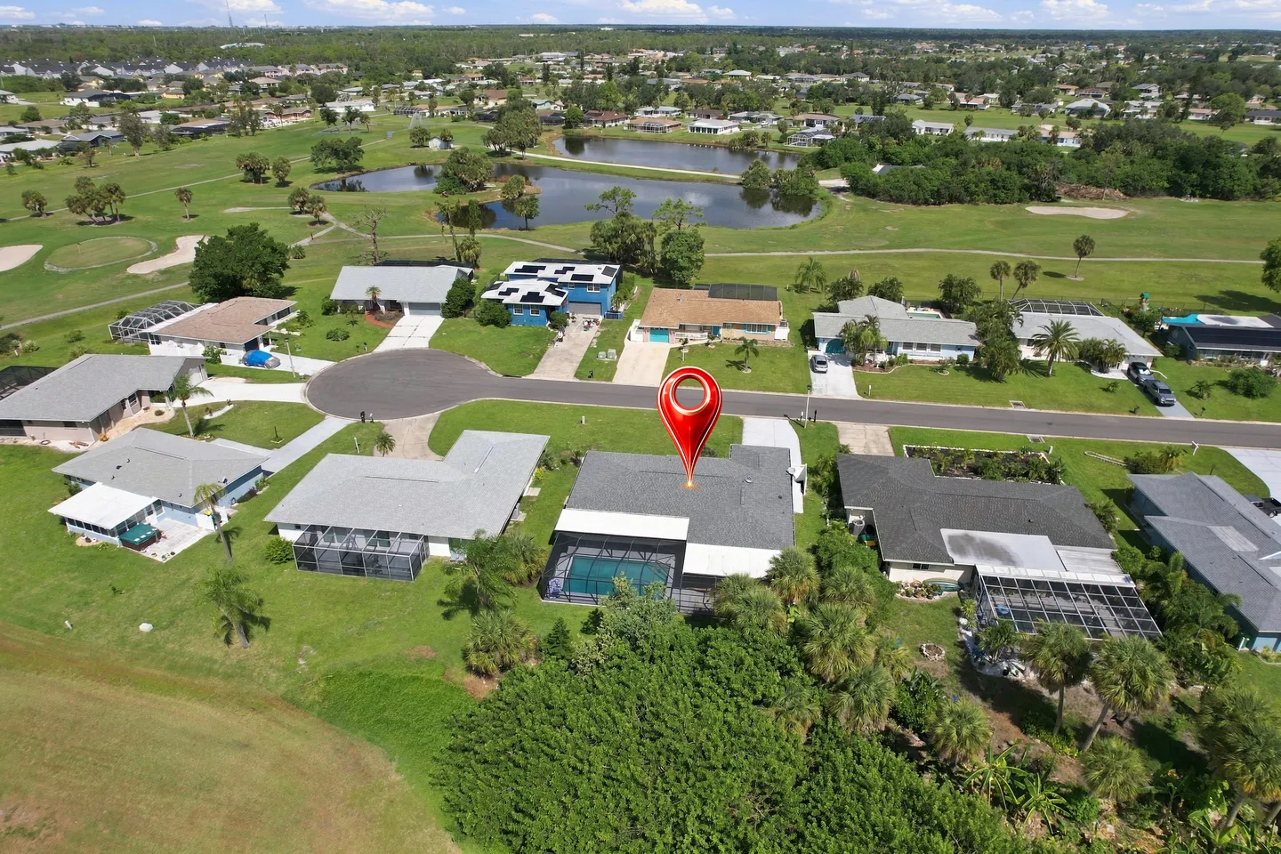 Aerial view of a suburban neighborhood showing a single-story house with a screened pool enclosure marked by a location pin, bordered by a golf course and ponds.