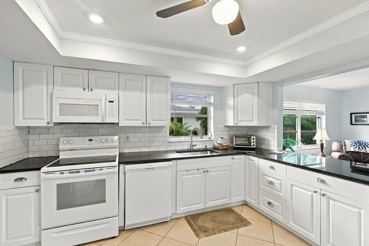 Bright kitchen featuring white cabinetry, dark countertops, white appliances, and a window above the sink.