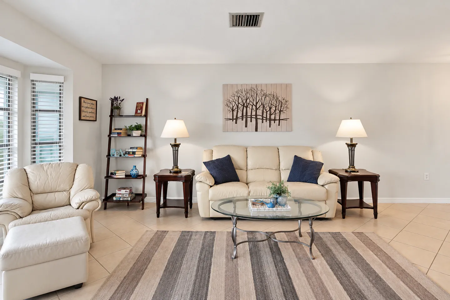 Living area with cream leather sofa, matching armchair and ottoman, striped area rug, and glass coffee table.