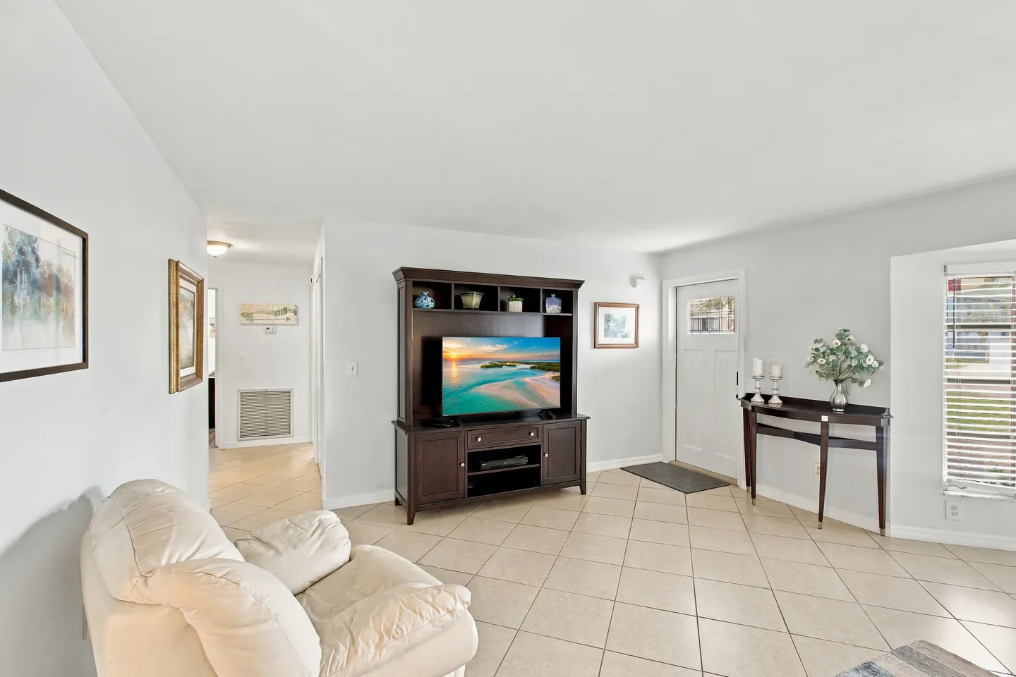 Living room with light-colored tile flooring, a dark wood entertainment center with a television, and a white front entry door.