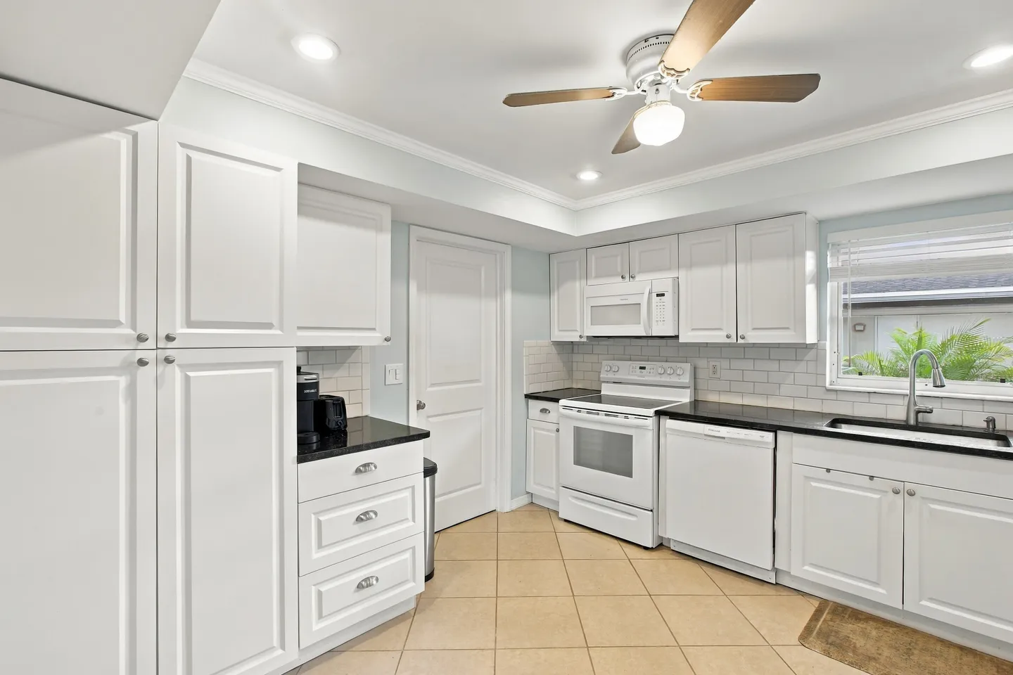 Kitchen featuring white cabinetry, dark countertops, white appliances, tiled flooring, and a ceiling fan.