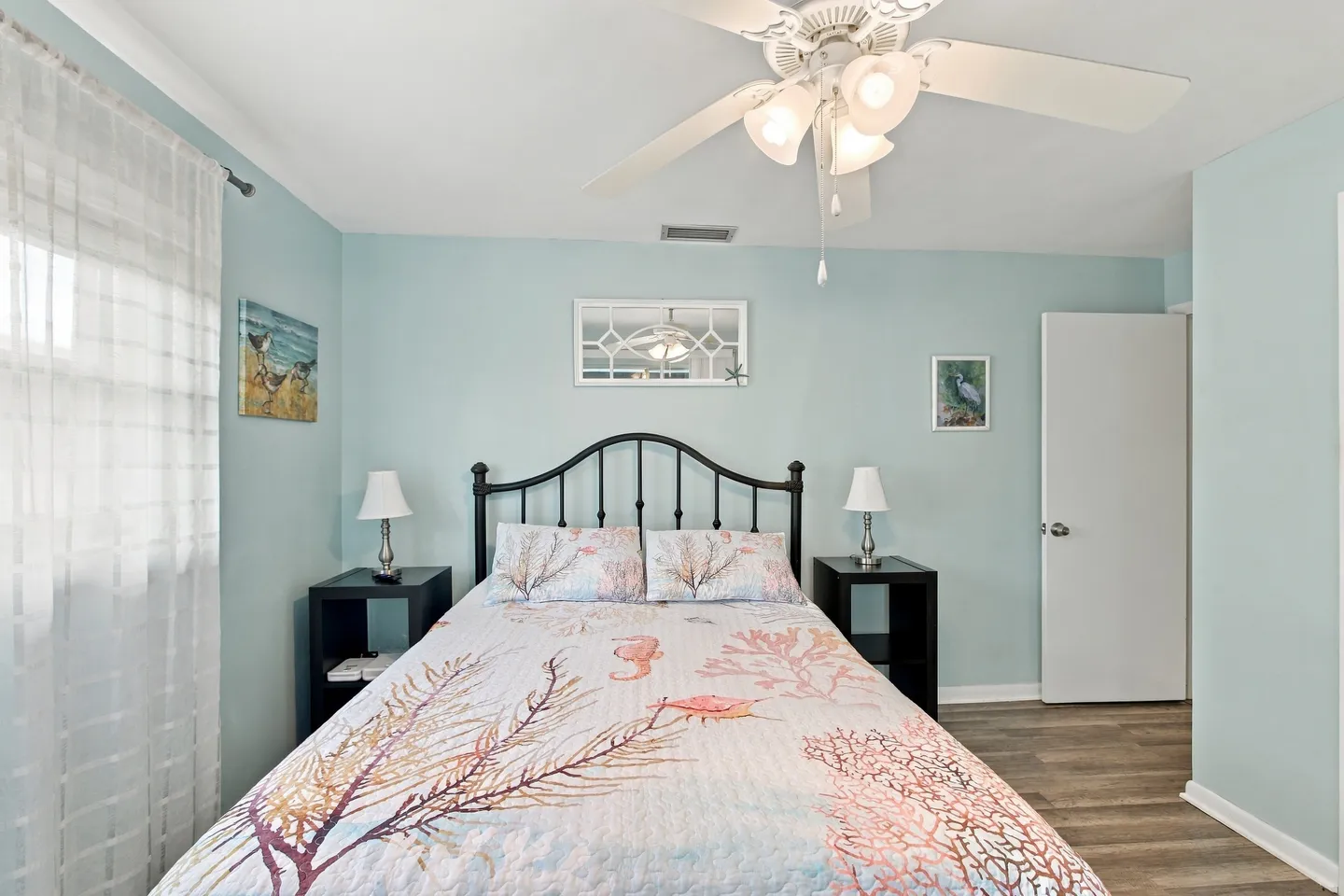Bedroom with light blue walls, a bed with a coastal-patterned bedspread, black metal headboard, and matching black nightstands.