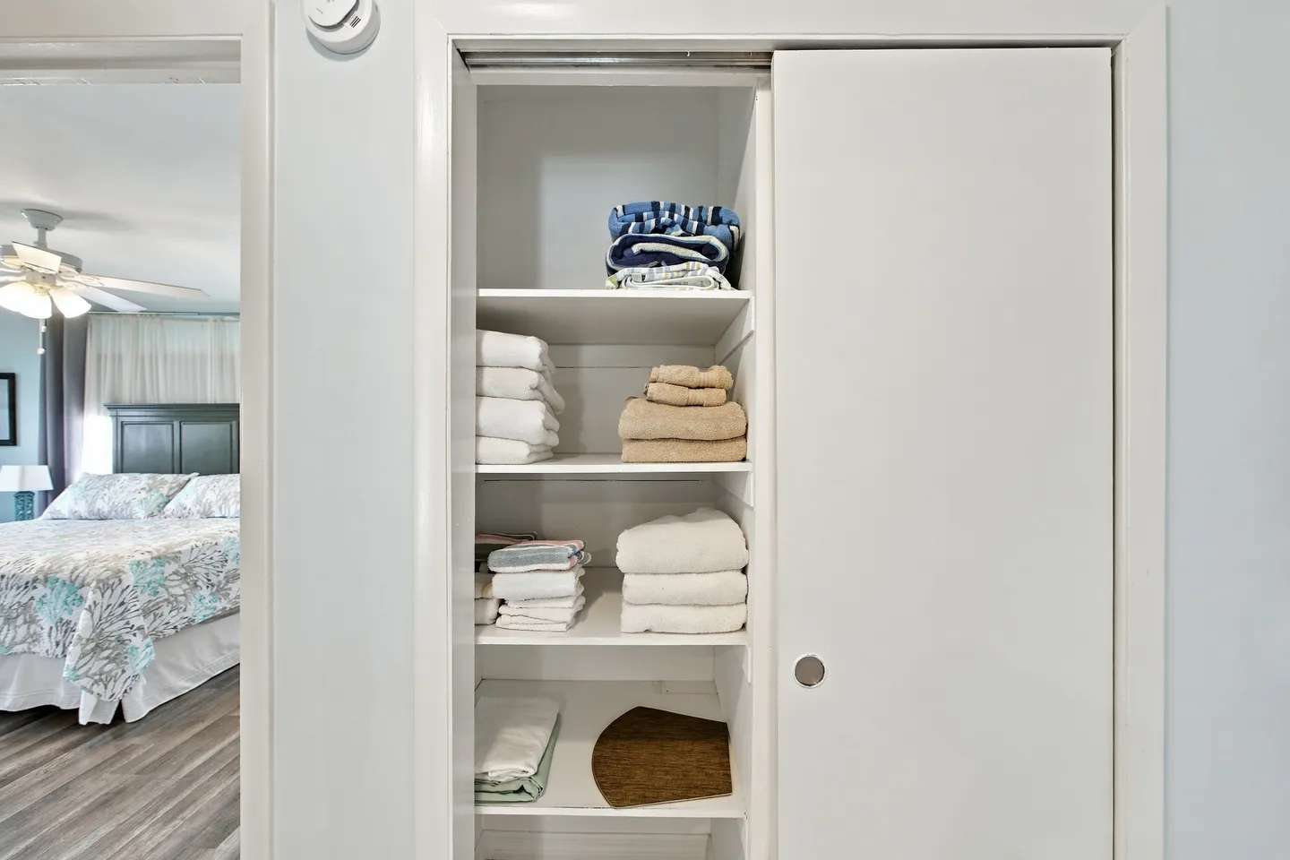 Open sliding closet door displaying stacked towels on built-in shelves next to a view into a bedroom.