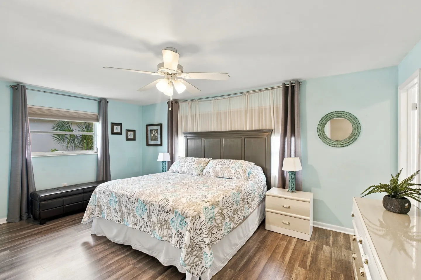 Bedroom with light blue walls, a bed with a floral patterned quilt, a wooden headboard, and a white ceiling fan.