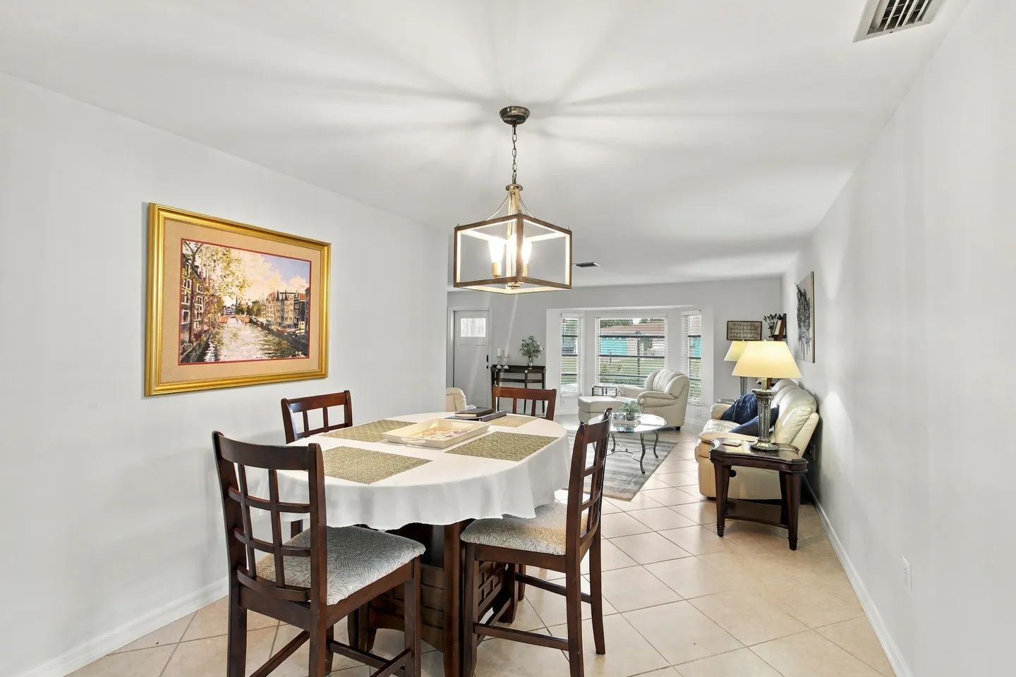 Dining area with a table and chairs leading into an open living room with light-colored tile flooring.