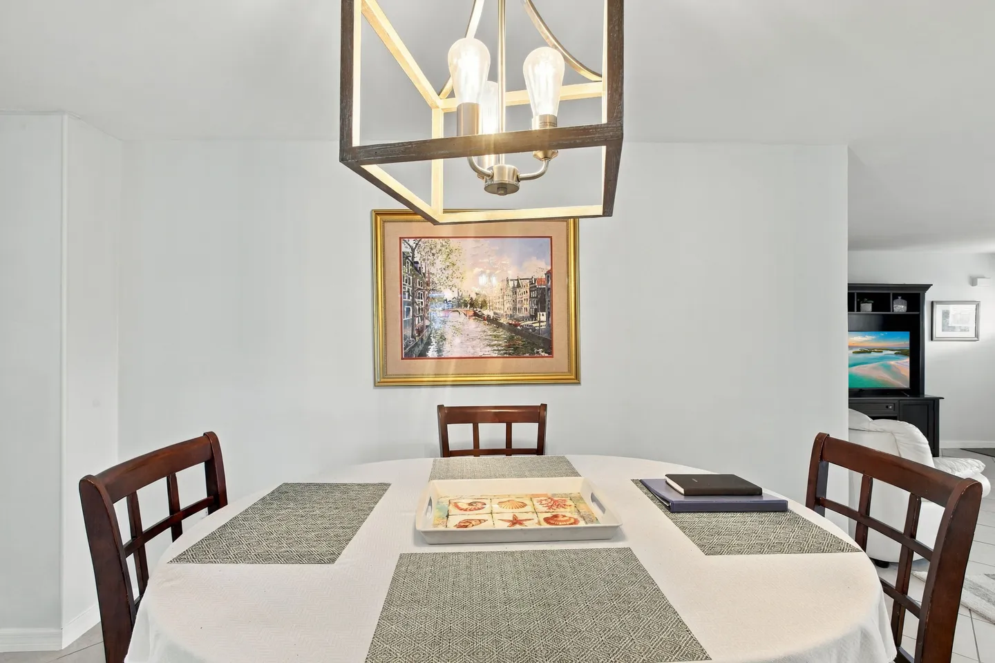 Dining area featuring a round table with placemats, wooden chairs, and an overhead geometric chandelier.