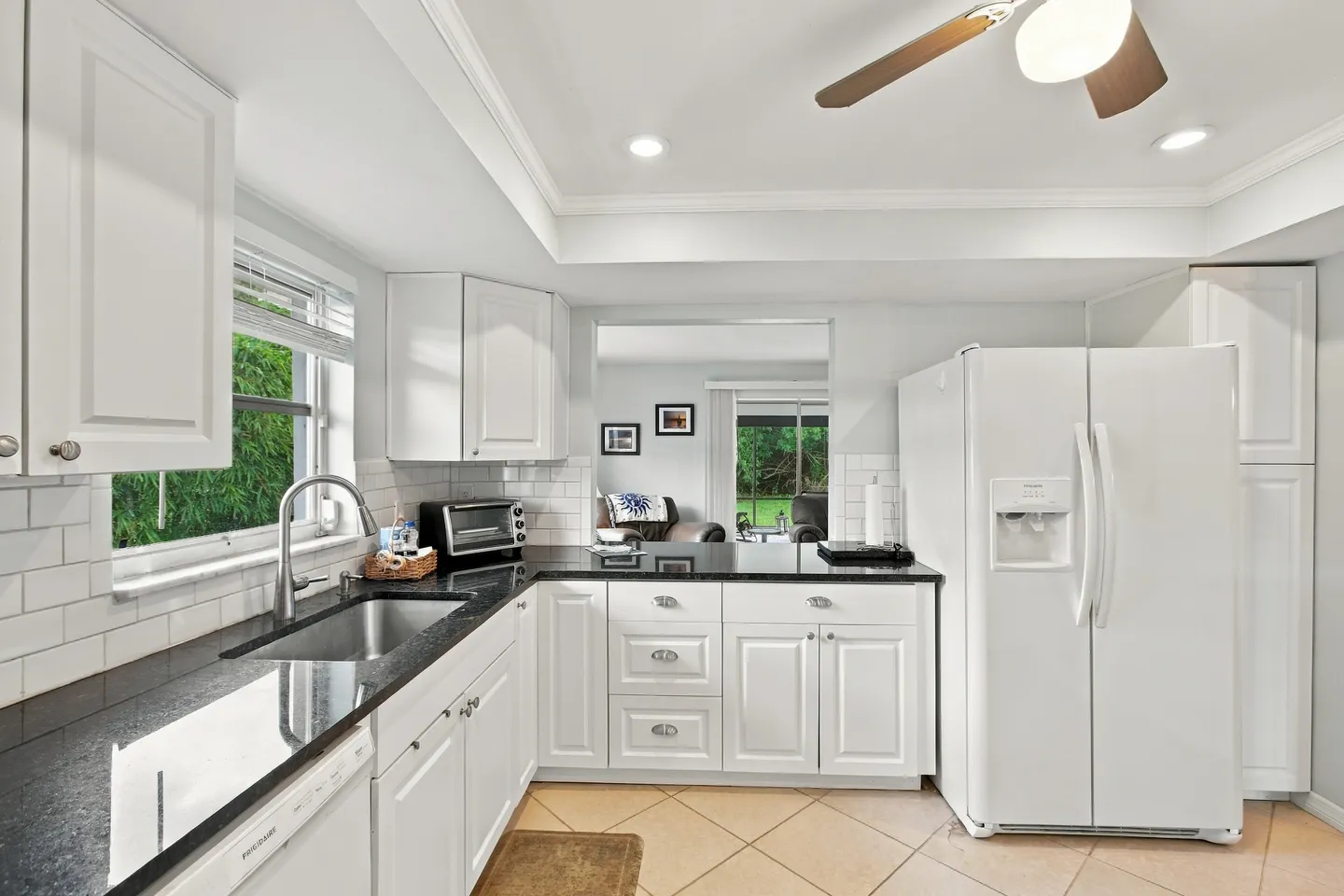 Kitchen with white cabinetry, dark countertops, a double-door white refrigerator, and a cutout pass-through view into an adjacent living area.