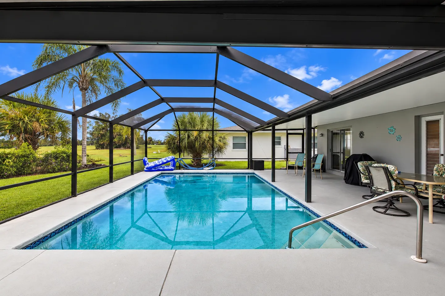 Rectangular swimming pool within a screened enclosure with views of a green lawn and trees under a blue sky.