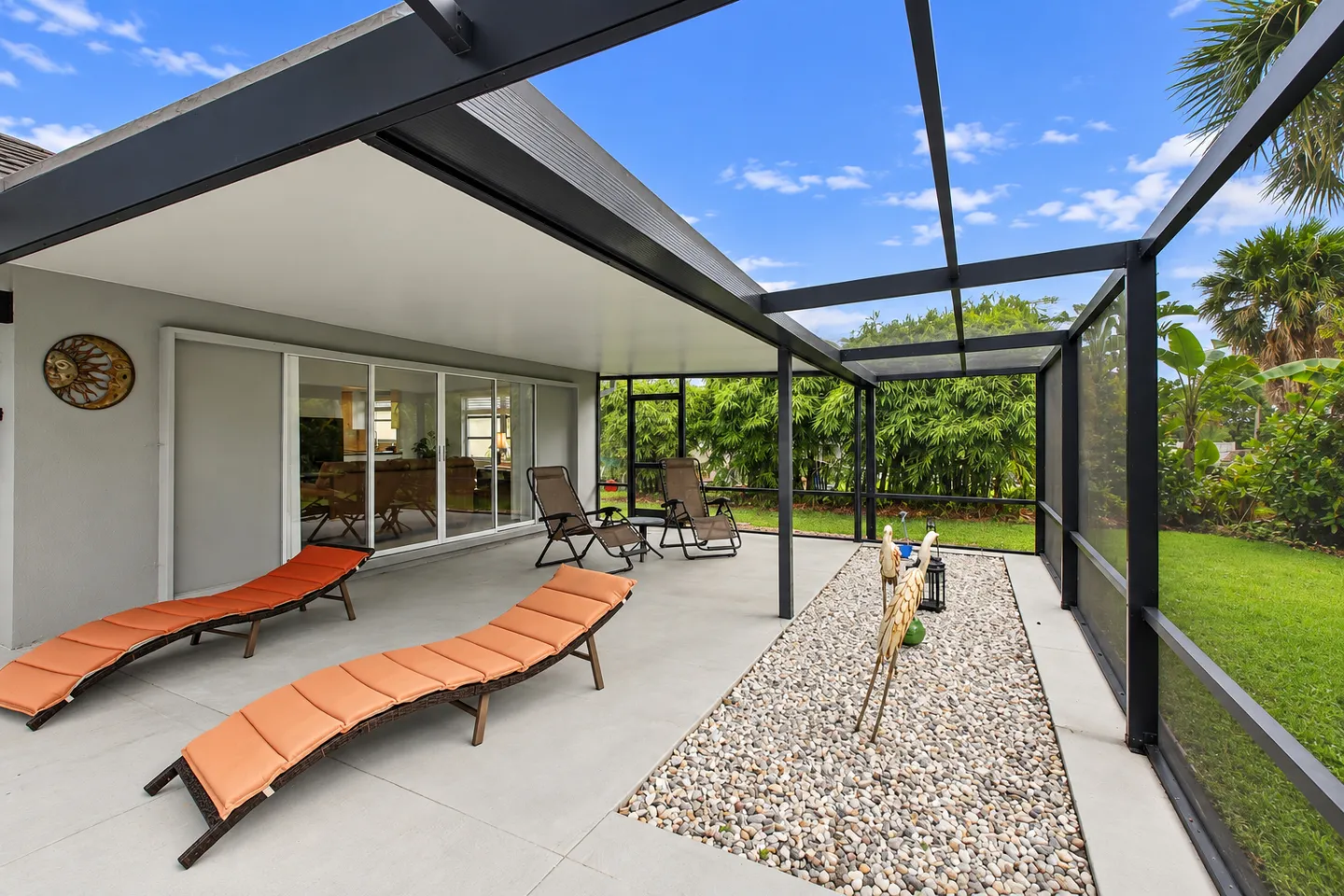 Screened-in patio with outdoor lounge chairs, a gravel bed, and a partially covered lanai facing a grassy yard.