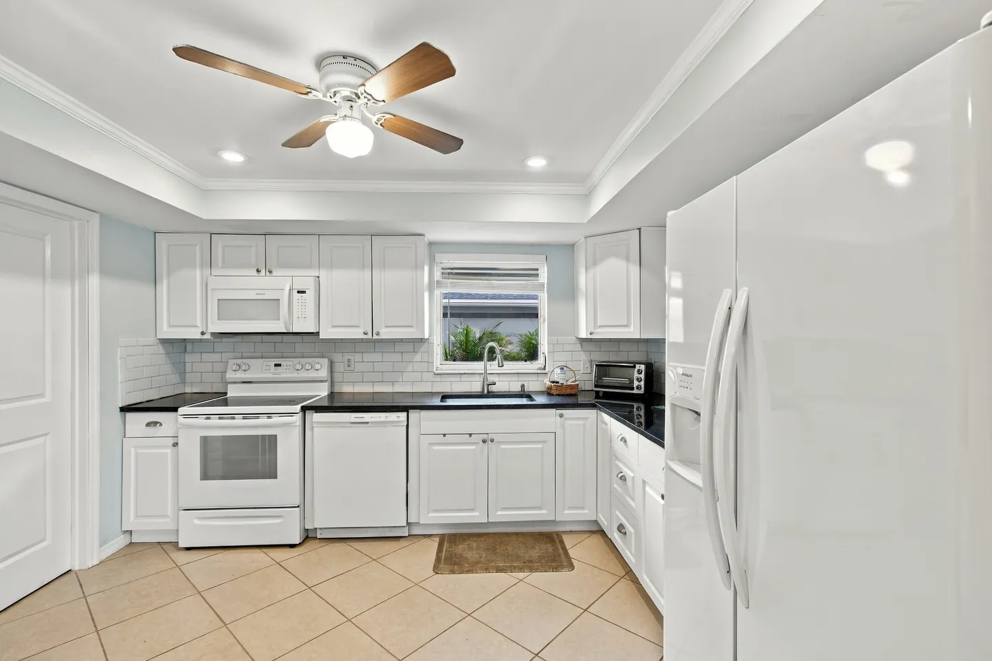 Kitchen with white cabinetry, dark countertops, white appliances, tiled flooring, and a ceiling fan.