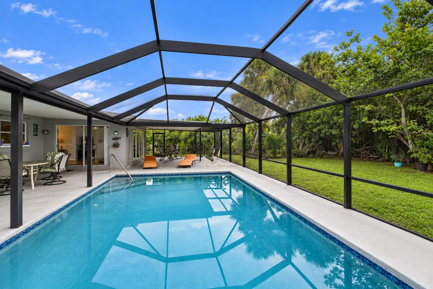 A rectangular swimming pool within a screened enclosure with patio seating and a grassy backyard visible outside.