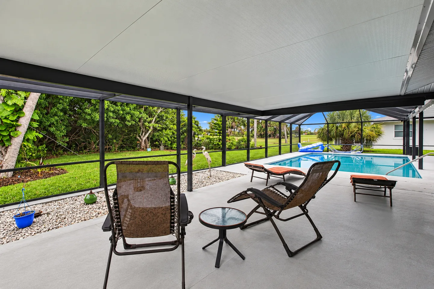 A covered patio with lounge chairs overlooking a swimming pool inside a screened enclosure.