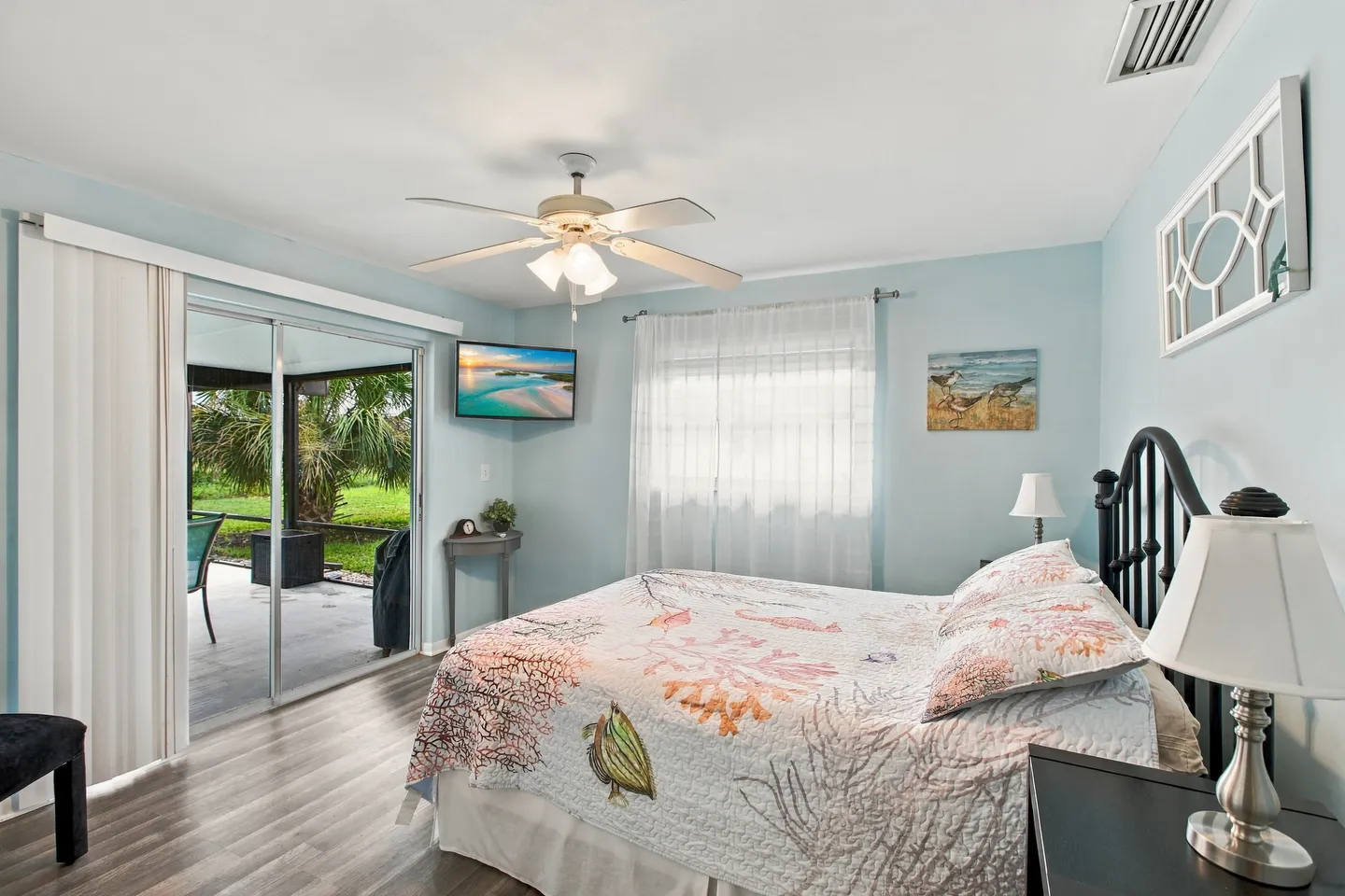Bedroom with coastal-themed bedding, a ceiling fan, a wall-mounted TV, and sliding glass doors leading to a covered patio.