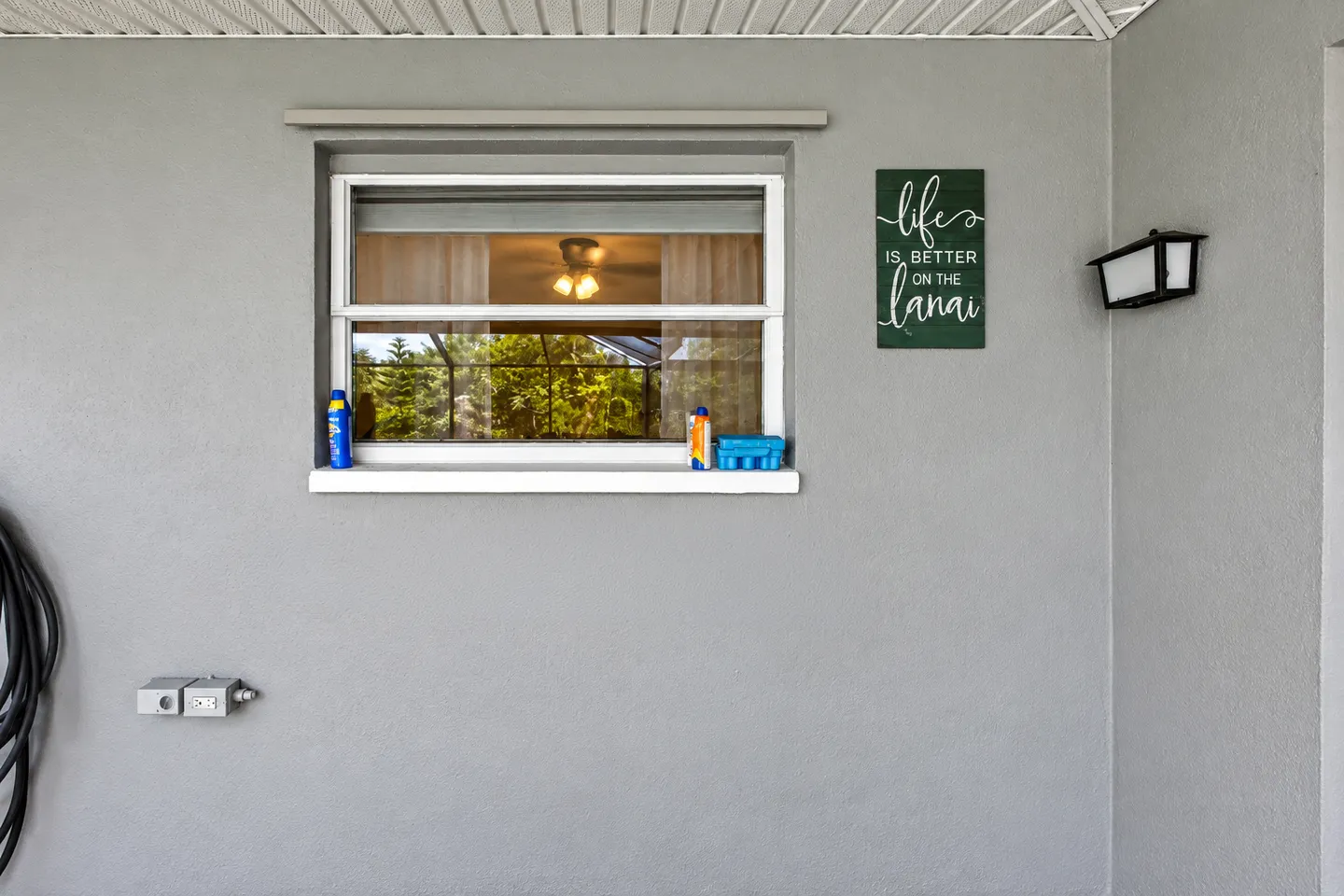 Exterior wall featuring a window with an interior ceiling fan visible, an outdoor light fixture, and decorative wall art.
