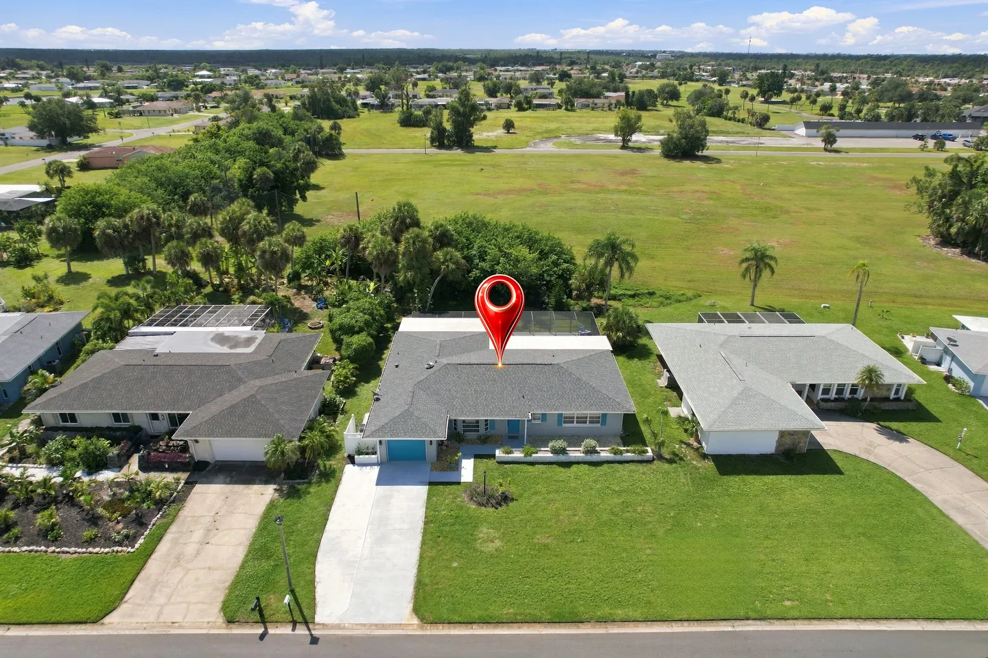Aerial view of a single-story house marked with a red map pin icon, featuring a concrete driveway and open green space in the backyard.
