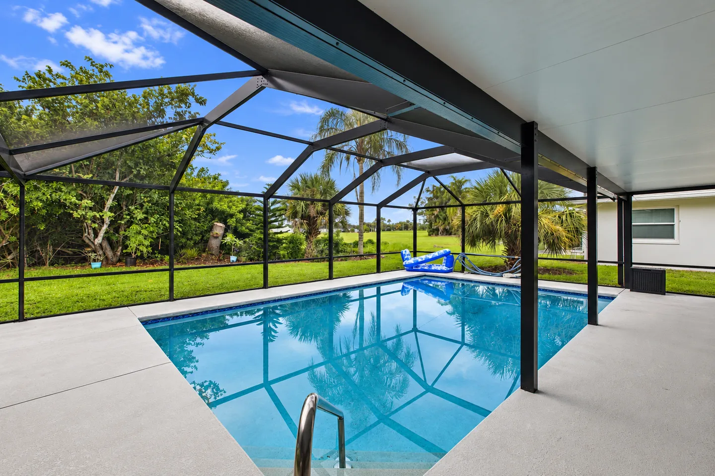 Screened-in outdoor swimming pool surrounded by a concrete patio overlooking a grassy backyard with trees.