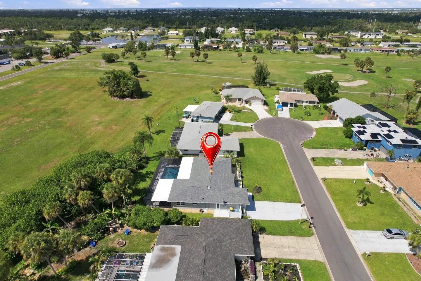 Aerial view of a residential neighborhood cul-de-sac with a red location pin over a single-story house backing onto an expansive green open space.