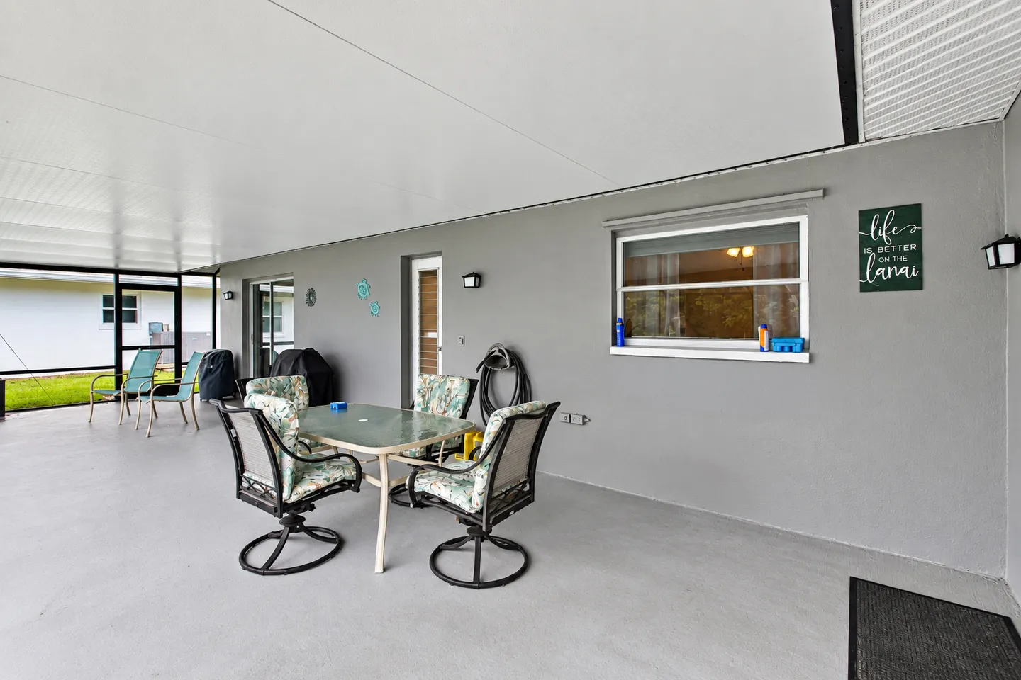 A covered screened-in patio with outdoor dining table, chairs, and grey walls.