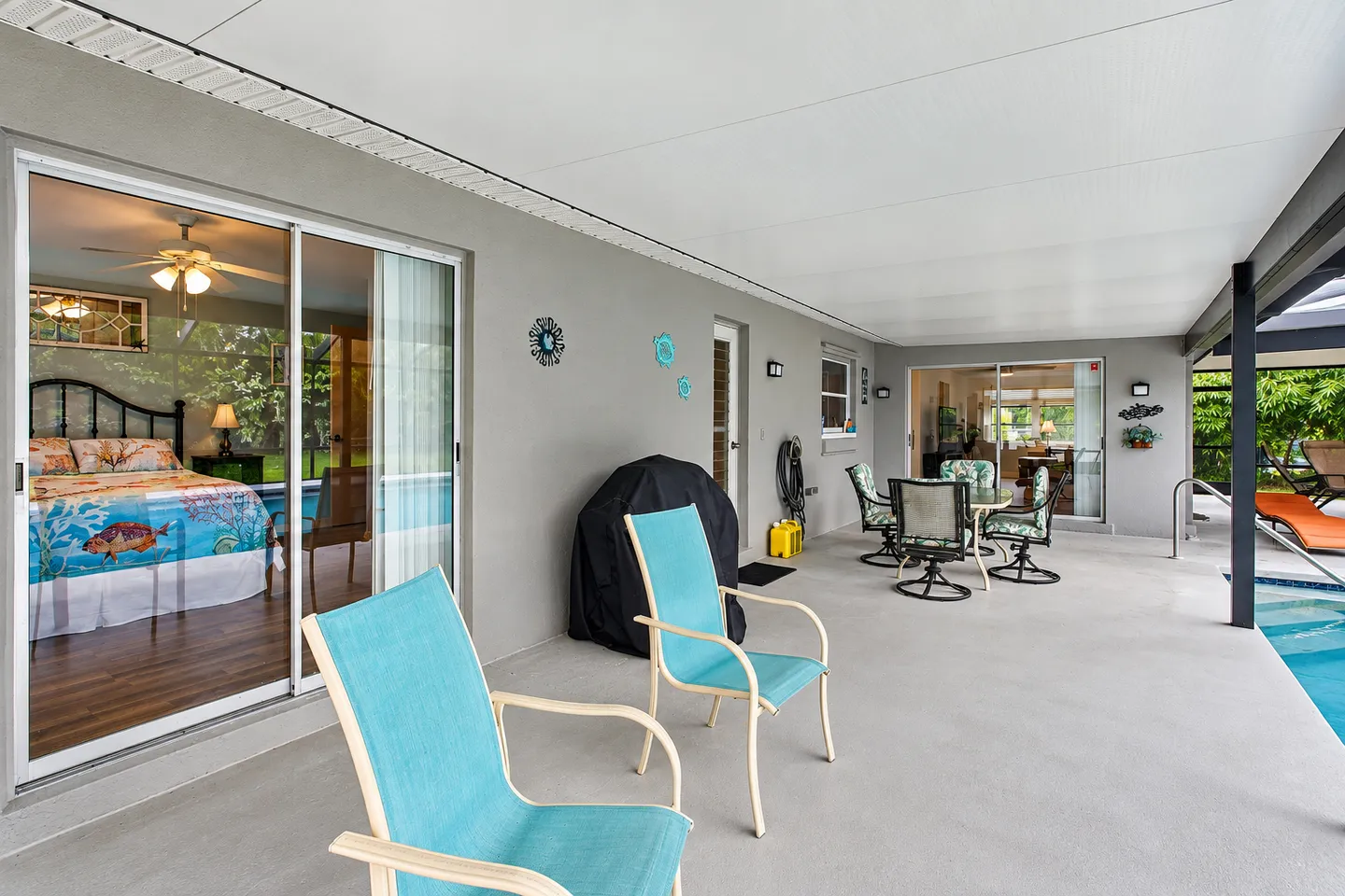Covered patio beside a swimming pool with seating and sliding glass doors leading indoors.