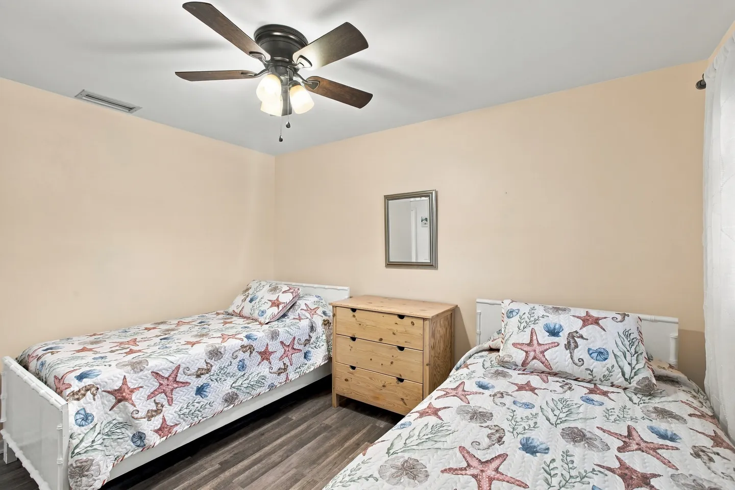 Bedroom with two twin beds dressed in sea-life bedding flanking a wooden dresser under a ceiling fan.
